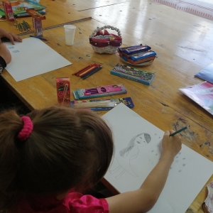 Dziewczynka rysuje kobietę w sukience na kartce papieru.