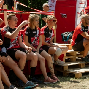 Grupa drużyny czerwono czarnych kibicują siedząc na ławce.