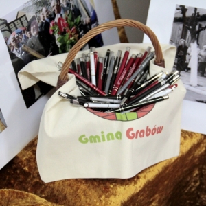 Koszyk ozdobiony logiem Gminy Grabów które jest przykryte długopisami.