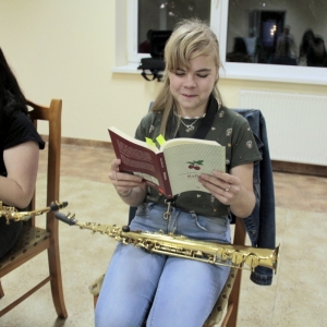 Dwie dziewczynki siedzące na krześle z instrumentem muzycznym na kolanach, czytają książkę pt. Balladyna".