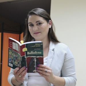 Pani Dyrektor Paulina Frontczak-Pawłowska patrzy w obiektyw trzymając w ręku książkę pt. Balladyna".