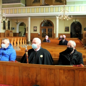Król palanta i inni ludzie siedzą w kościele z maseczkami ochronnymi.