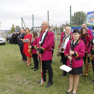 Grupka osób z Gminnej Orkiestry Dętej stoi na trawniku trzymając swoje instrumenty muzyczne.