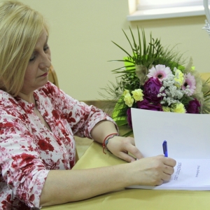 Pani Anna Bobrowicz podczas składania autografu w otwartej książce.