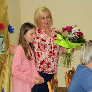 Uśmiechnięta Pani Anna Bobrowicz trzymająca bukiet kolorowych kwiatów stoi obok uśmiechniętej dziewczynki. 