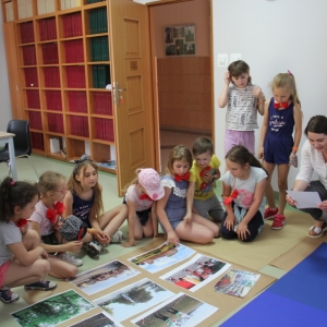 Pani Dyrektor GCKB przykucnięta z grupką dzieci, wybierają kolorowe obrazki spośród tych, które są ułożone na podłodze.