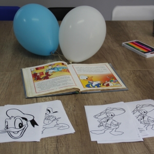 Kolorowanki i książka Kaczora Donalda wraz z kredkami i balonikami leżące na stole.