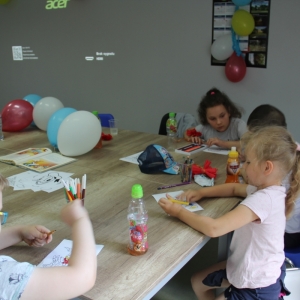 Grupka dzieci siedząca przy stolikach, koloruje kolorowanki z Kaczorem Donaldem. 