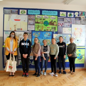 Pani Dyrektor Paulina Frontczak-Pawłowska pozuje razem z dziećmi do zdjęcia, w tle kolorowe prace plastyczne.