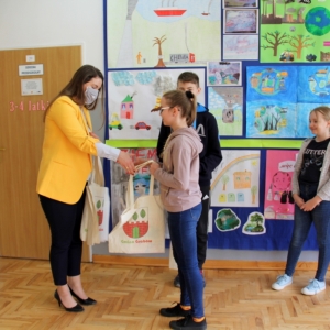 Pani Dyrektor Paulina Frontczak-Pawłowska wręcza dziewczynce torbę z logiem Gminy Grabów, w tle kolorowe prace plastyczne.