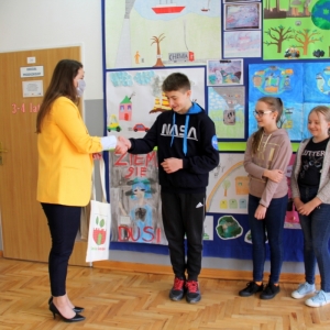 Pani Dyrektor Paulina Frontczak-Pawłowska gratuluje chłopcy i podaje mu torbę z logiem Gminy Grabów, w tle kolorowe prace plastyczne.
