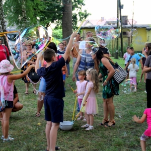 Dzieci puszczające ogromne bańki mydlane podczas imprezy w plenerze wraz z innymi uczestnikami.