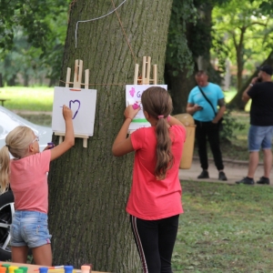 Dwie dziewczynki malują na kartkach przyczepionych drewnianymi spinaczami do drzewa.