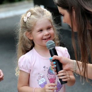 Uśmiechnięta dziewczynka rozmawia z Panią Dyrektor GCKB Grabów trzymającą mikrofon. 