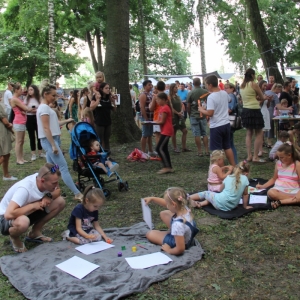 Dwie grupki dzieci malujących obrazki, a w tle tłum gości pikniku.