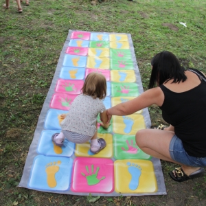 Mała dziewczynka z mamą podczas zabawy w grze ułożonej na trawie.