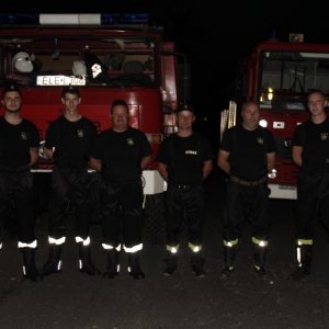 Zdjęcie grupowe sześciu strażaków na tle dwóch wozów strażackich.