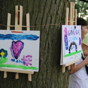 Dwie prace namalowane przez dzieci, zaczepione na drzewie drewnianymi spinaczami.