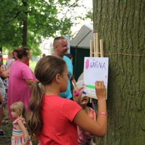 Dziewczynka malująca na kartce przyczepionej drewnianymi spinaczami do drzewa.