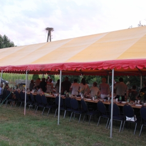 Stoły zapełnione gośćmi na Wiejskim Pikniku Rodzinnym w Byszewie, pod żółtym namiotem.