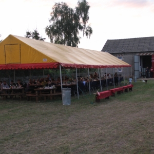 Stoły zapełnione gośćmi na Wiejskim Pikniku Rodzinnym w Byszewie, pod żółtym namiotem.