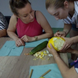 Pani prowadzącej pomaga uczestniczce w wycinania wzorów w melonie.