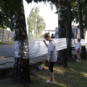 Dwie dziewczynki malują flamastrami na folii przymocowanej do drzew.