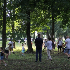 Grupka dzieci i rodziców bawiąca się między drzewami na terenie pikniku.