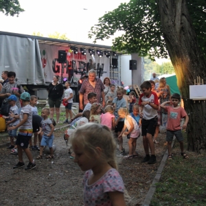 Grupka dzieci podczas zabawy zorganizowanych przez animatorkę na tle sceny podczas pikniku.