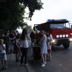Grupka dzieci z rodzicami przy wozie strażackim.