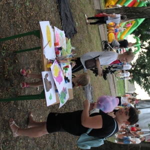 Dzieci z mamą przy stoisku do malowania farbami.