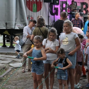 Grupa dzieci podczas zorganizowanej przez animatorkę zabawy na tle sceny podczas pikniku.