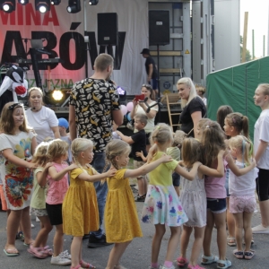 Grupka dzieci podczas tańców i zabawy wraz z animatorką przed sceną na pikniku.