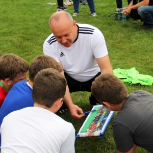 Trener pokazuje dzieciom klub piłkarski na boisku.
