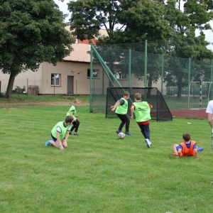 Dwie drużyny chłopców z różnymi znacznikami grają w piłkę nożną na boisku.
