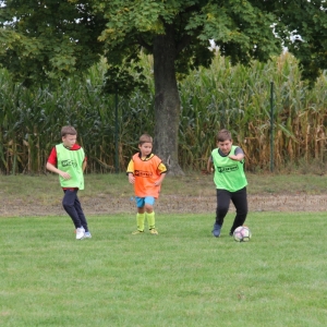 Trzech chłopców w różnych znacznikach biegnie za piłką na boisku.
