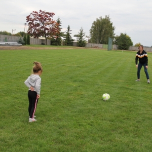 Dziewczynka stoi na przeciwko pani a pomiędzy nimi jest piłka na boisku.