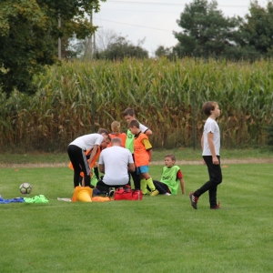 Dzieci w znacznikach pochylają się nad trenerem na boisku.