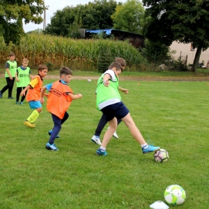 Dwie drużyny chłopców z różnymi znacznikami grają w piłkę nożną na boisku.