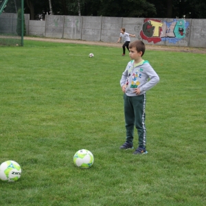 Chłopiec stoi na boisku z rękoma położonymi na biodrach a przed nim leżą trzy piłki.