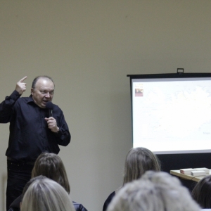 Pan Roman Pankiewicz podczas spotkania autorskiego w Grabowie stoi na tle rzutnika przed grupą osób siedzących w sali.