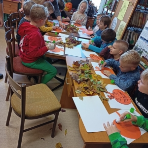 Dzieci siedzą przy stołach i robią ozdoby jesienne.