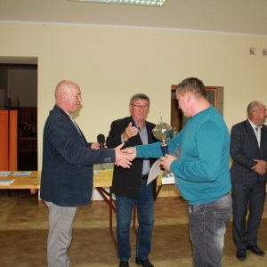 Uśmiechnięty pan z Polskiego Związku Hodowców Gołębi podczas otrzymywania pucharu wraz z gratulacjami.