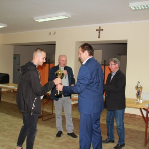 Uśmiechnięty pan z Polskiego Związku Hodowców Gołębi podczas otrzymywania pucharu wraz z gratulacjami.