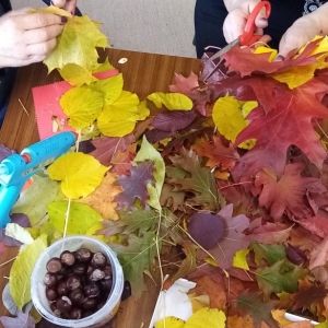 Panie stoją przy stole pełnym liści w kolorach jesiennych i robią ozdoby.