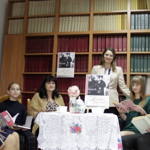 Pani Dyrektor Paulina Frontczak-Pawłowska wraz z uczestnikami siedzą przy stoliku trzymając książki i patrzą w obiektyw.