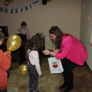 Pani Dyrektor Paulina Frontczak-Pawłowska wręcza pierwszej dziewczynce z kolejki torebkę z nagrodami, a dziewczynka mówi do mikrofonu. 