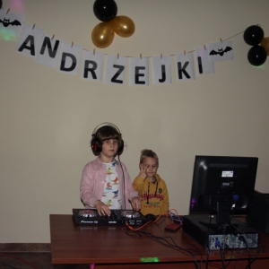 Dwaj chłopcy na tle dekoracji z napisem „Andrzejki", stoją przy sprzęcie didżeja.