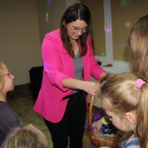 Pani Dyrektor Paulina Frontczak-Pawłowska częstuje dzieci upominkami z kosza wiklinowego.