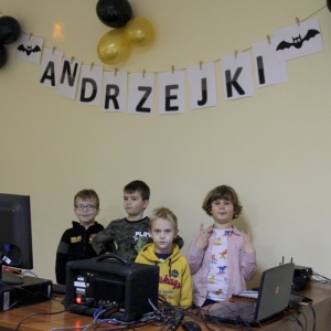 Czterej chłopcy na tle dekoracji z napisem „Andrzejki", stoją przy sprzęcie didżeja.